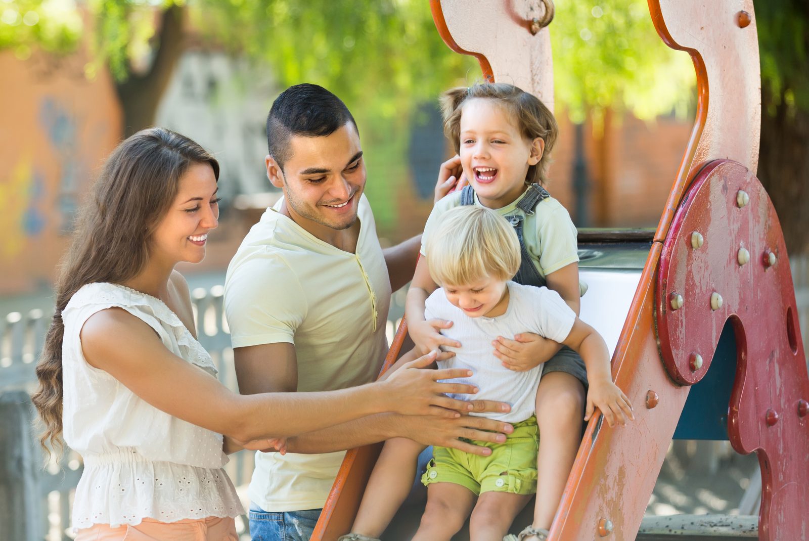 Familie mit zwei Kindern an einer Rutsche auf dem Spielplatz
